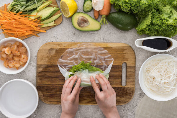 top view of woman making roll on cutting board among ingredients 