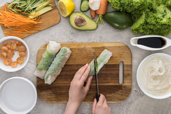 top view of woman cutting with knife spring rolls on cutting board 