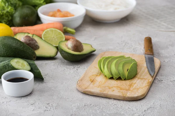 Gesneden Avocado Snijplank Met Mes Onder Rauwe Ingrediënten — Stockfoto