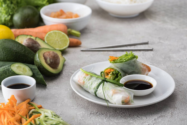  tasty spring rolls with soy sauce on white plate with metal sticks 