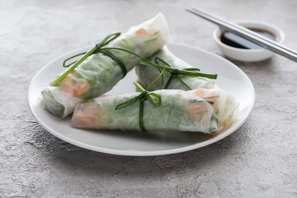 tasty and served spring rolls with on white plate with soy sauce and metal sticks