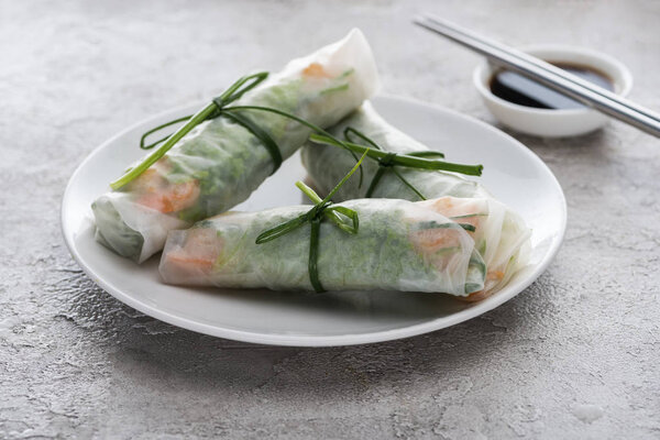 tasty and served spring rolls with on white plate with soy sauce and metal sticks 