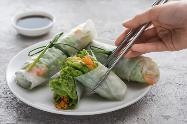 cropped view of woman eating tasty spring rolls with metal sticks