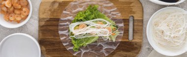panoramic shot of shrimps, lettuce and noodles on rice paper, on cutting board  clipart