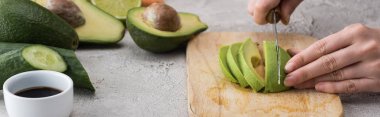 panoramic shot of woman cutting avocado with knife on cutting board among ingredients  clipart