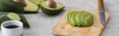 panoramic shot of cut avocado on cutting board with knife among raw ingredients  clipart