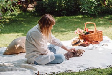 sarışın kız bahçede beyaz battaniye oturan ve sevimli köpek yavrusu ile güneşli bir gün piknik