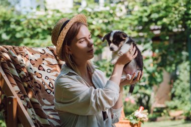bahçede güverte sandalyede otururken saman şapka tutan Galce Corgi köpek yavrusu sarışın kız