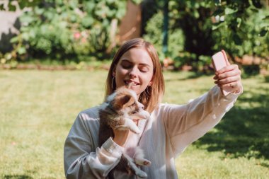 bahçede sevimli Galce Corgi köpek yavrusu ile selfie alarak mutlu sarışın kız