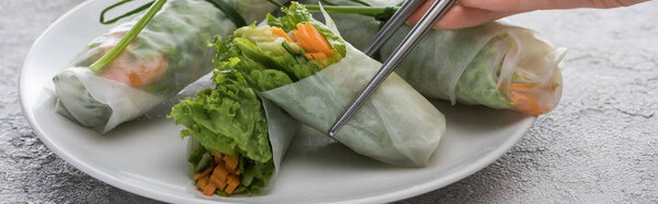 panoramic shot of woman holding tasty spring roll with metal sticks 