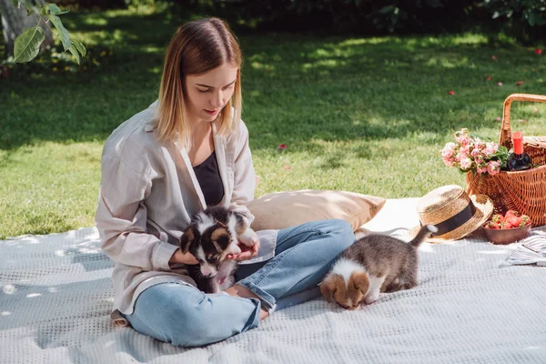 庭の白い毛布に座って かわいい子犬と晴れた日にピクニックを持っている魅力的なブロンドの女の子 — ストック写真