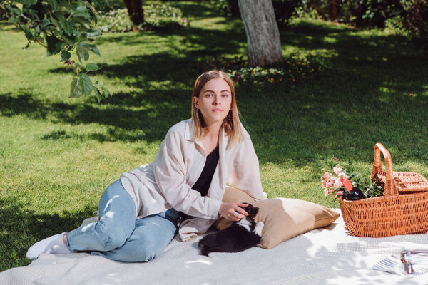 attractive blonde girl sitting on white blanket in garden with adorable welsh corgi puppy