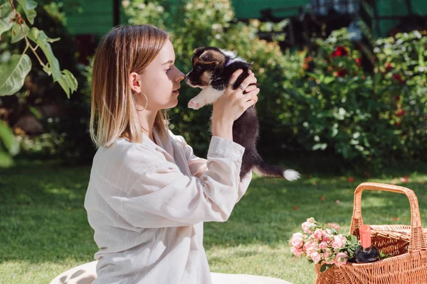 かわいいウェールズのコーギー子犬と庭で魅力的なブロンドの女の子の側面図 — ストック写真