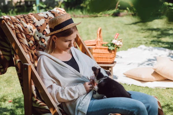 ピクニック中に庭のデッキチェアに座っている間 子犬を保持するわら帽子のブロンドの女の子 — ストック写真