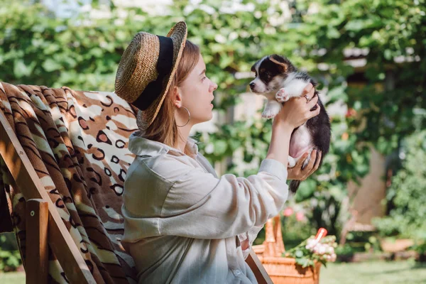 庭のデッキチェアに座っている間 子犬を保持するわら帽子のブロンドの女の子の側面図 — ストック写真
