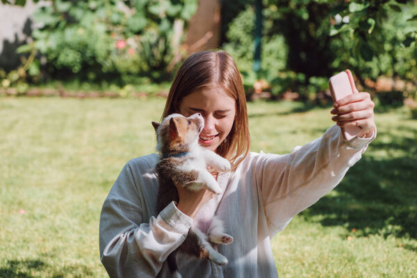 smiling blonde girl taking selfie with cute welsh corgi puppy in garden