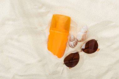 orange bottle of sunscreen on sand with seashells and stylish sunglasses clipart
