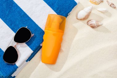 orange bottle of sunscreen on sand with seashells, striped towel and sunglasses clipart