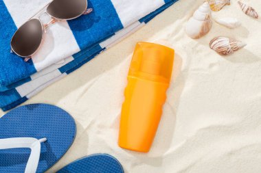 bottle of sunscreen on sand near striped towel, blue flip flops, sunglasses and seashells clipart