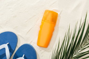 mavi Flip flop ile kum üzerinde yeşil palmiye yaprağı yakın turuncu güneş kremi