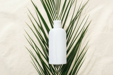 white sunscreen lotion on green palm leaf on sand clipart