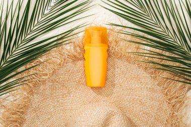 top view of stylish straw hat on golden sand with green palm leaves and sunscreen clipart