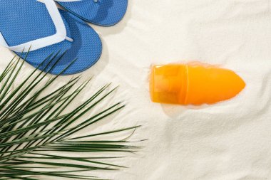 Altın kumda güneş kremi, palmiye yaprağı ve Flip flop üst görünümü