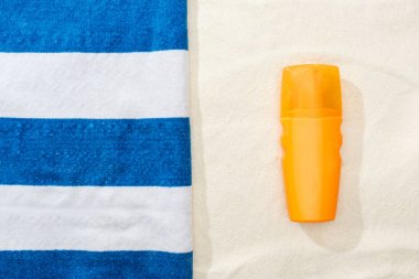 altın kum üzerinde güneş koruyucu ve çizgili mavi ve beyaz havlu üst görünümü