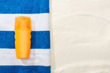 kum üzerinde güneş kremi ve çizgili mavi ve beyaz havlu üst görünümü