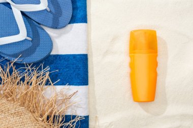 Güneş kremi, saman şapka, Flip flop ve altın kum üzerinde çizgili mavi ve beyaz havlu üst görünümü