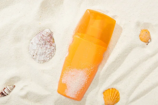 貝殻と砂の上の日焼け止めのオレンジ色のボトル — ストック写真