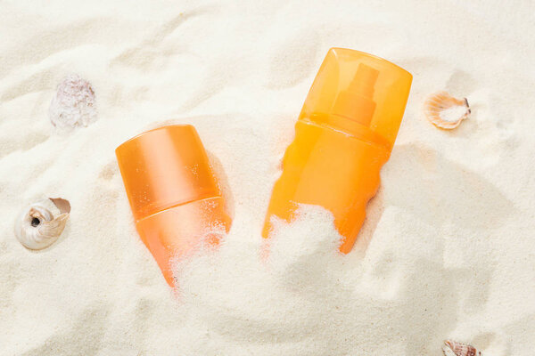 orange bottles of sunscreen in sand near seashells