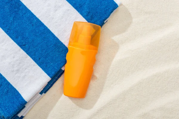 Orangefarbene Flasche Sonnencreme Auf Sand Mit Gestreiftem Handtuch — Stockfoto