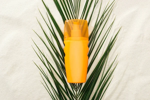 橙色防晒霜化妆水在沙上的绿棕榈叶上 — 图库照片