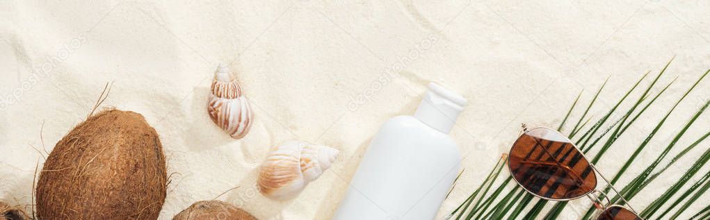 top view of seashells, coconuts and sunscreen lotion, sunglasses and palm leaf on sand, panoramic shot