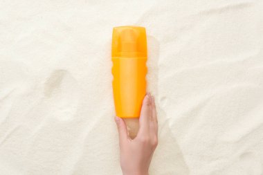 cropped view of woman holding orange sunscreen lotion above golden sand clipart