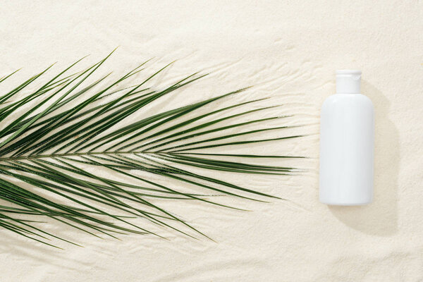 white sunscreen lotion near green tropical leaf on sand