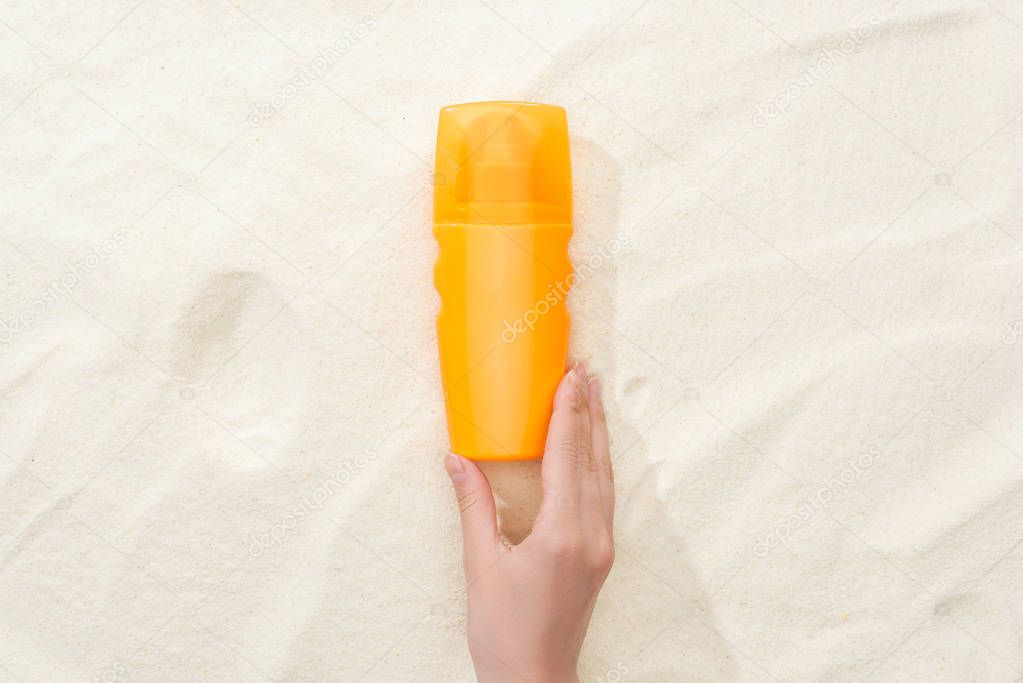 cropped view of woman holding orange sunscreen lotion above golden sand