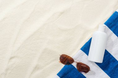 güneş gözlüğü üst görünümü, kum çizgili havlu ve beyaz losyon