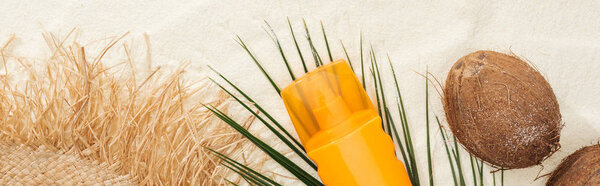 top view of palm leaf, coconuts and sunscreen product with straw hat on sand, panoramic shot