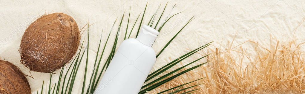 top view of palm leaf, sunscreen, coconuts and straw hat on sand, panoramic shot