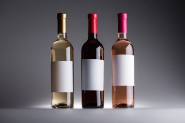 gri arka planda boş etiketlerle beyaz, kırmızı ve gül şarabı şişeleri