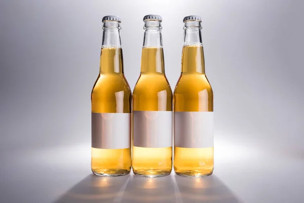 Τρία Γυάλινα Μπουκάλια Μπύρα Λευκές Ετικέτες Γκρίζο Φόντο — Φωτογραφία Αρχείου