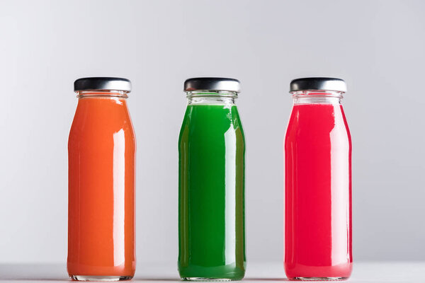 row of glass bottles with multicolored juice isolated on grey