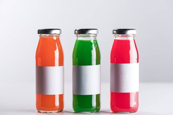 row of glass bottles with multicolored liquid and white blank labels isolated on grey