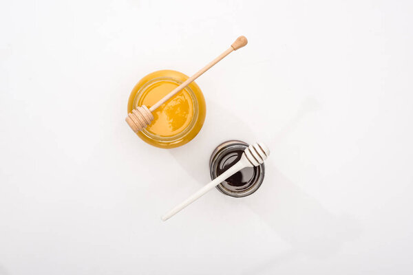 top view of jars with honey and wooden honey dippers on white background with copy space