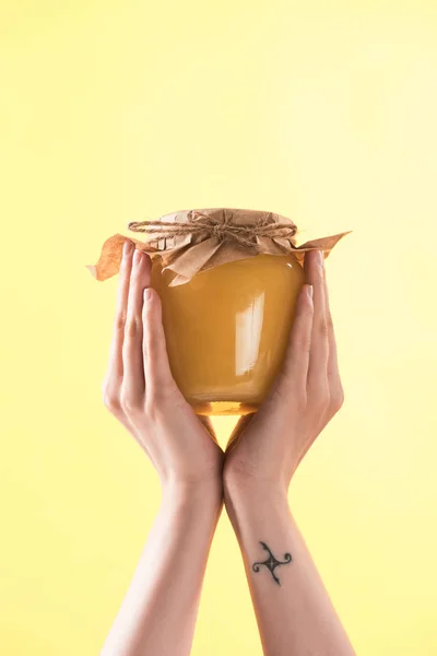 黄色に隔離された蜂蜜でガラス瓶を持つ女性のトリミングされたビュー — ストック写真