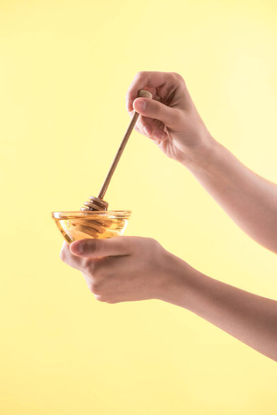 cropped view of woman holding glass bowl and wooden dipper with honey isolated on yellow