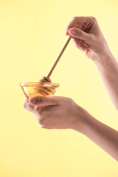 cropped view of woman holding glass bowl and wooden dipper in honey isolated on yellow