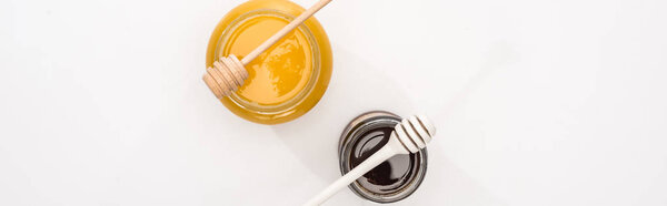 panoramic shot of jars with honey and honey dippers on white background